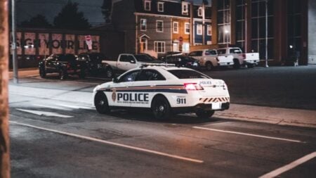 A police car drives through an urban street at night illuminated by streetlights.
