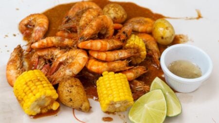 New York Subway Rider Eats Seafood Boil With Her Hands as Sauce Drips All Over the Floor: ‘This Is Stinking Up the Whole Train’ Appetizing seafood boil featuring shrimp, corn, potatoes, and lime wedges.