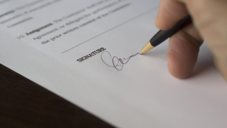 California Notary Says Former Employer Used Their Stamp and Signature After They Quit: ‘This Is Straight Up Forgery’ A hand signs a formal contract with a pen on a wooden desk