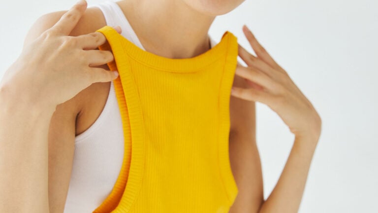 Woman indoors holding a bright yellow tank top