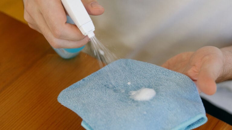 ‘He’s a Christian Nationalist’: Pennsylvania Worker Says Boss Brushed Off Coworker Bringing ‘Incredibly Contagious’ Illness to Work Close-up of hands using disinfectant spray and cloth on a wooden table