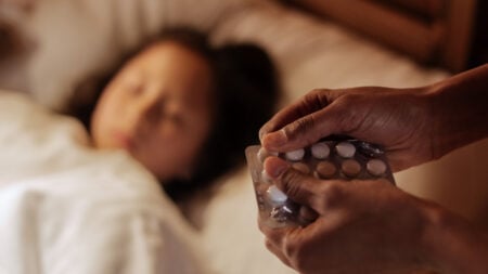 A mother holding pills beside her sick daughter lying in bed