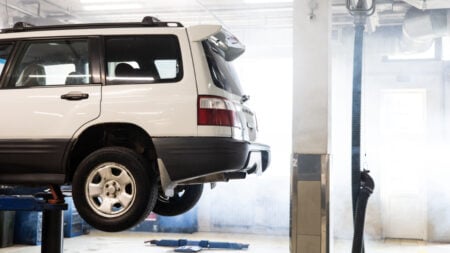 California Car Owner Says Mechanic Is Holding Car Hostage After $2,100 in Unauthorized Repairs: ‘He Refused To Give Me My Keys’ white SUV is elevated on a lift inside an auto repair shop for maintenance