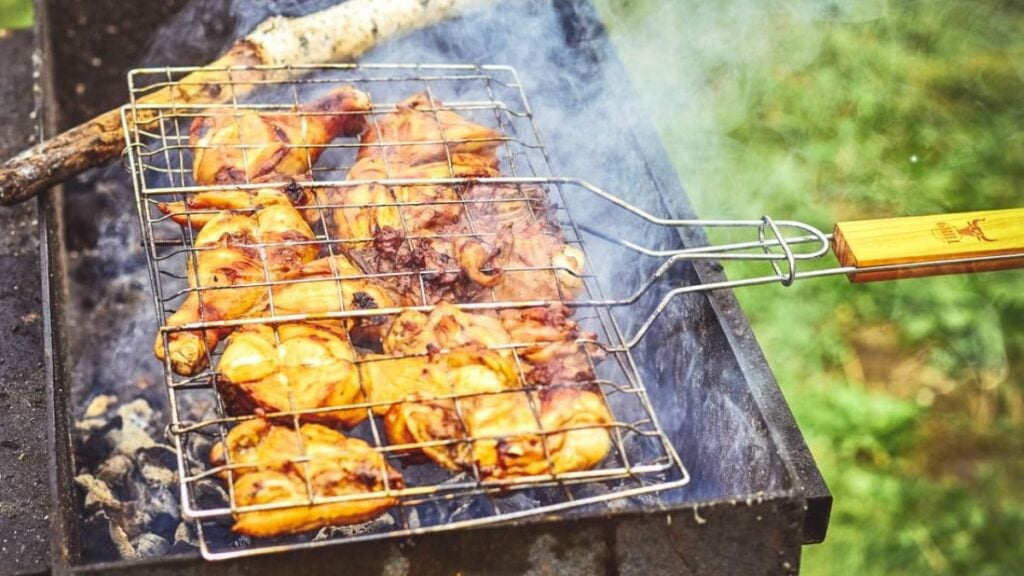 Illinois Man Fires Up Charcoal Grill and Starts Cooking Chicken Wings Inside Moving CTA Train: ‘There’s No Shortage of Stupid’ Close-up of grilled chicken on an outdoor barbecue, emitting smoke and flavor.