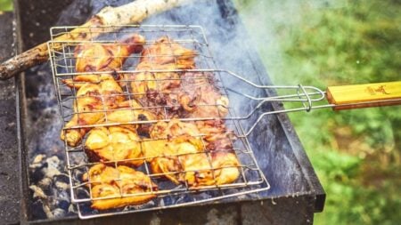 Close-up of grilled chicken on an outdoor barbecue, emitting smoke and flavor.