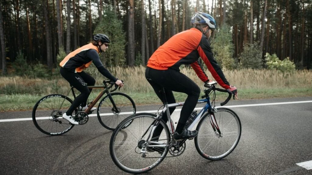 Two cyclists in vibrant gear biking along a forest road, enjoying a leisurely ride.