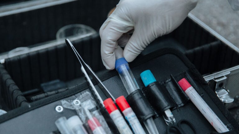 Gloved hand handling test tube in forensic equipment case