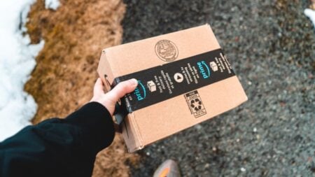 California MAGA Grandma Points Weapon at Hispanic Amazon Driver, Refuses to Back Down After He Identifies Himself: ‘Mental Illness’ A person holding a cardboard Amazon Prime package on a snowy urban sidewalk.
