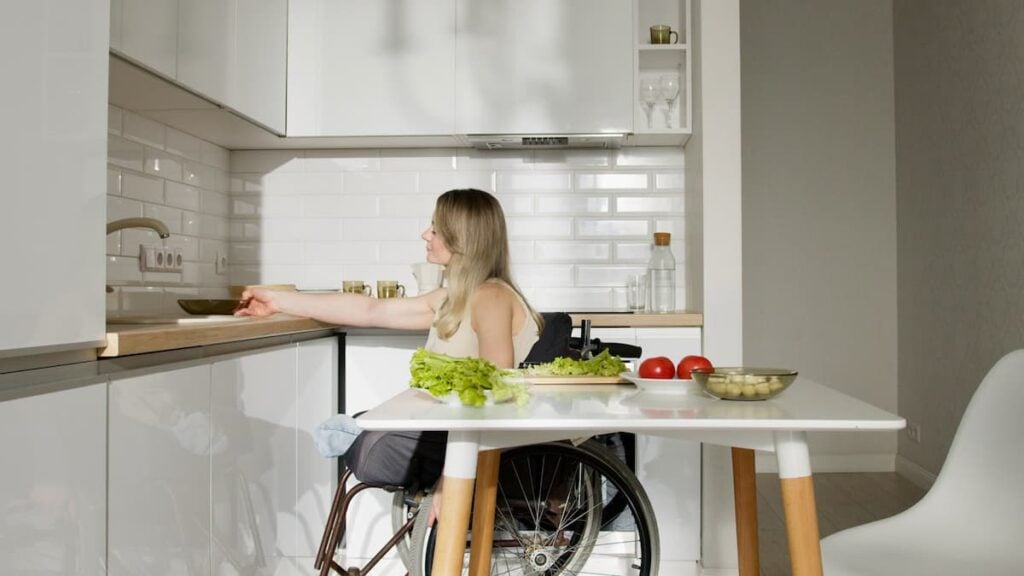 ‘I Feel Totally Betrayed’: Disabled Florida Residents Say Hope Florida Failed Them as $10 Million Controversy Deepens Woman in wheelchair preparing food in a modern kitchen with fresh vegetables.