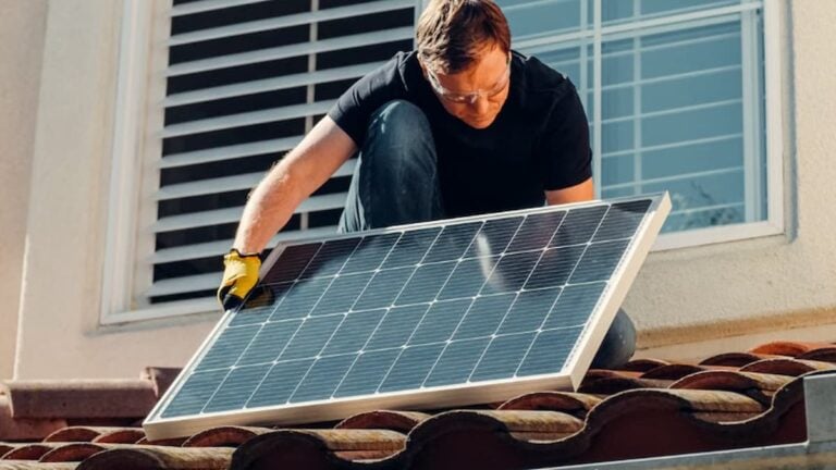 A worker installing a solar panel on a residential rooftop under bright sunlight.