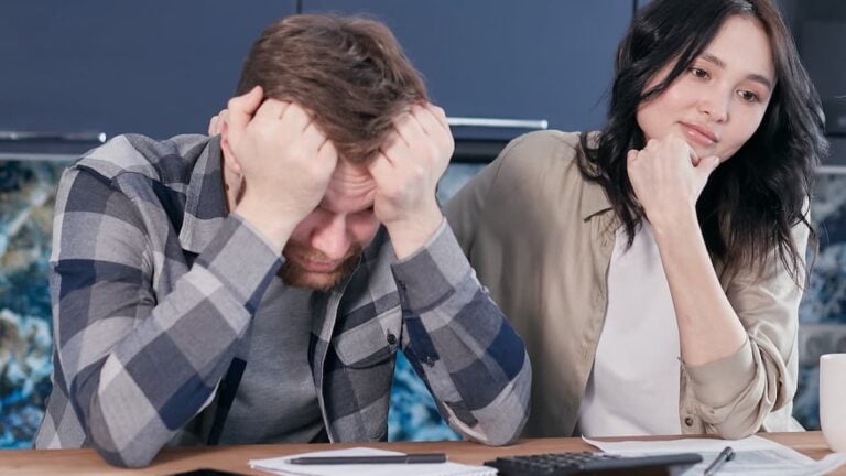 A couple looking worried while reviewing financial documents at a kitchen table.