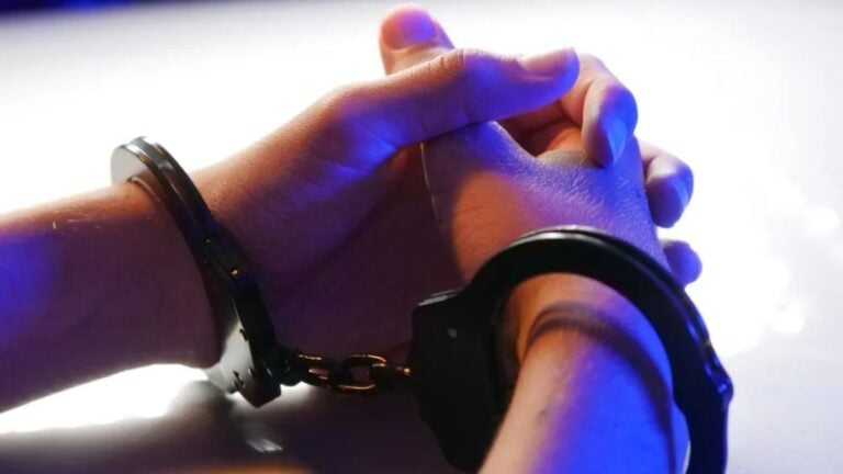 Texas Police Drag Elderly Hispanic Woman Across Ground During Son’s Arrest: ‘Inhuman Treatment Of An Old Lady’ Close-up of handcuffed hands under blue police light, signifying arrest or detention.