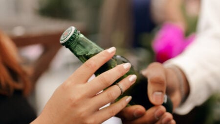 A close-up image of two people exchanging a green beer bottle at a social gathering
