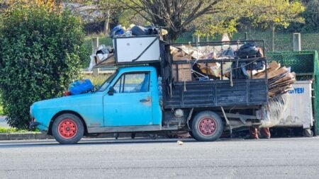 Florida Customer Refuses to Pay Junk Hauler, So He Dumps All Their Debris Right Back on the Driveway: ‘Driver Should Get a Medal’ Side view of a vintage blue truck loaded with recyclable waste on a sunny day.