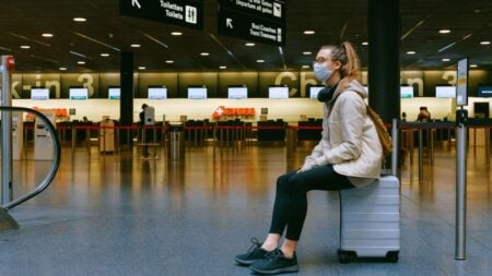 A woman wearing a face mask sits on luggage in an airport terminal amid the pandemic.