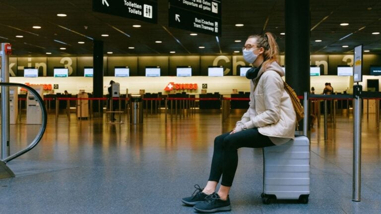 A woman wearing a face mask sits on luggage in an airport terminal amid the pandemic.