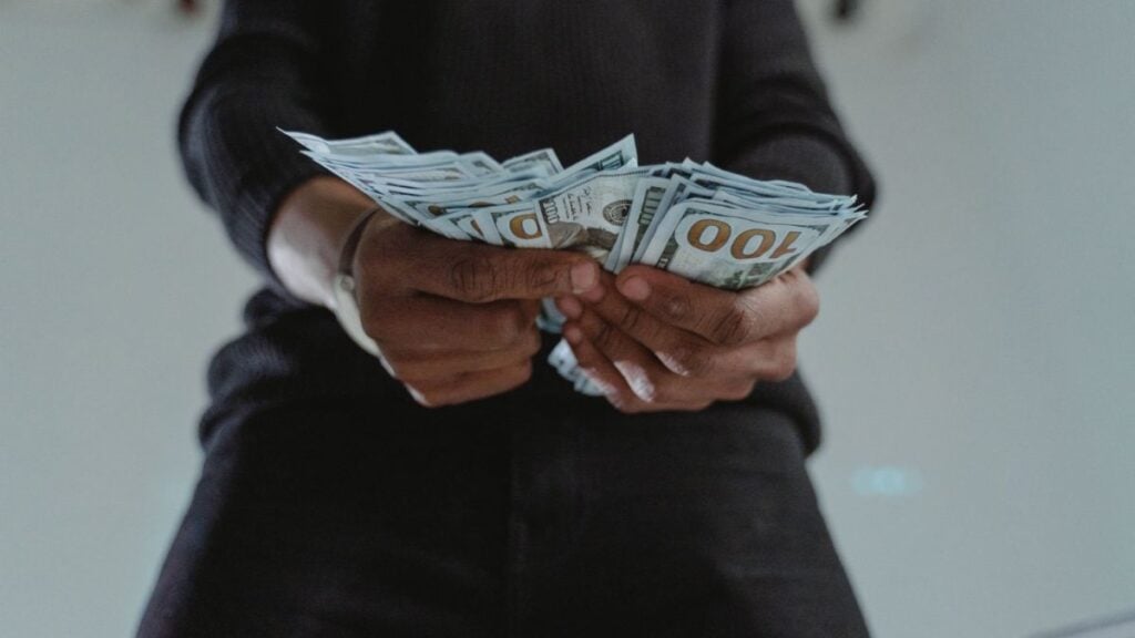 New York Mom and Friends Face Backlash for Allegedly Attacking Daughter Over $5K Theft: ‘There’s a Way to Go About Things’ A close-up view of a person holding a stack of US hundred dollar bills indoors.