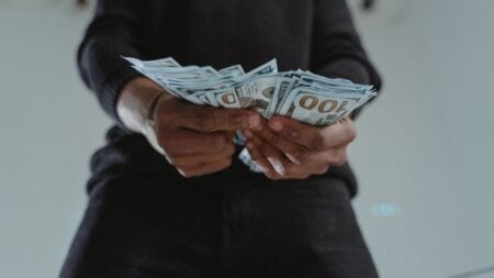 A close-up view of a person holding a stack of US hundred dollar bills indoors.