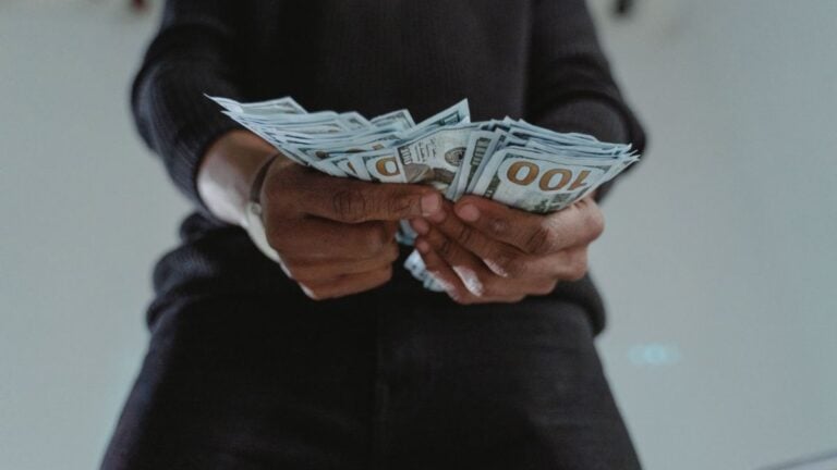 A close-up view of a person holding a stack of US hundred dollar bills indoors.