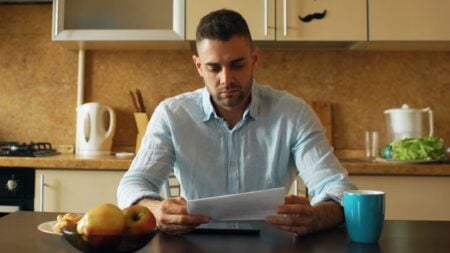 Upset young man reading letter with unpaid bill in the kitchen at home eraly morning