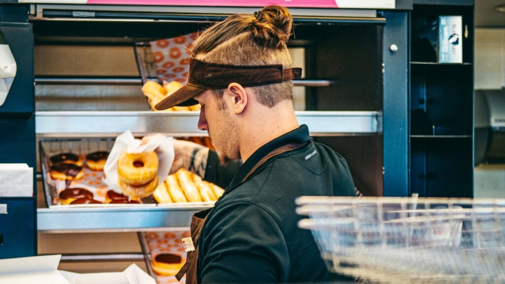 ‘He Straight Up Lied to Me’: Pennsylvania Woman Says Dunkin’ Donuts Manager Tried to Trick Her After Mistaking Her for DoorDasher Back view of an employee in a donut shop serving freshly baked donuts to customers