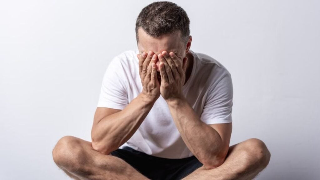 Michigan Dad Breaks Down Over Financial Struggles as Pranksters Joke About Stealing Money From Him: ‘This Is Not “Content.” It’s Sick’ A man sits cross-legged with his face hidden in hands, conveying stress or contemplation.