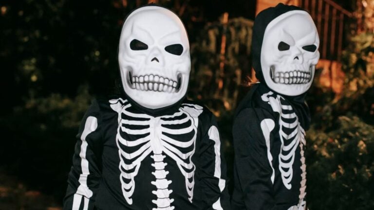 Two children dressed in skeleton costumes enjoying Halloween night outdoors.